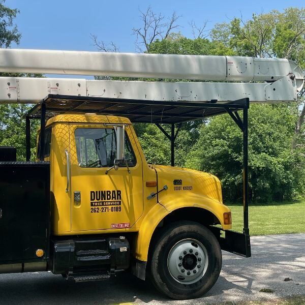 Yellow boom truck from Dunbar Tree Service with tree trimming equipment, parked in a green outdoor setting, showcasing professional tree care capabilities in Waukesha County.