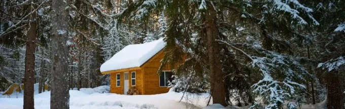 Cozy wooden cabin surrounded by snow-covered trees in a winter forest.