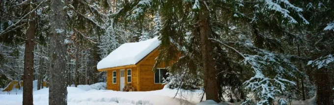 Cozy wooden cabin surrounded by snow-covered trees in a winter forest.